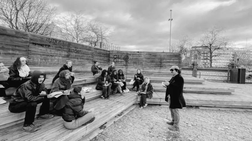 Nicolás Bronzina leading an outdoor session with a group of students seated on wooden steps, notebooks in hand